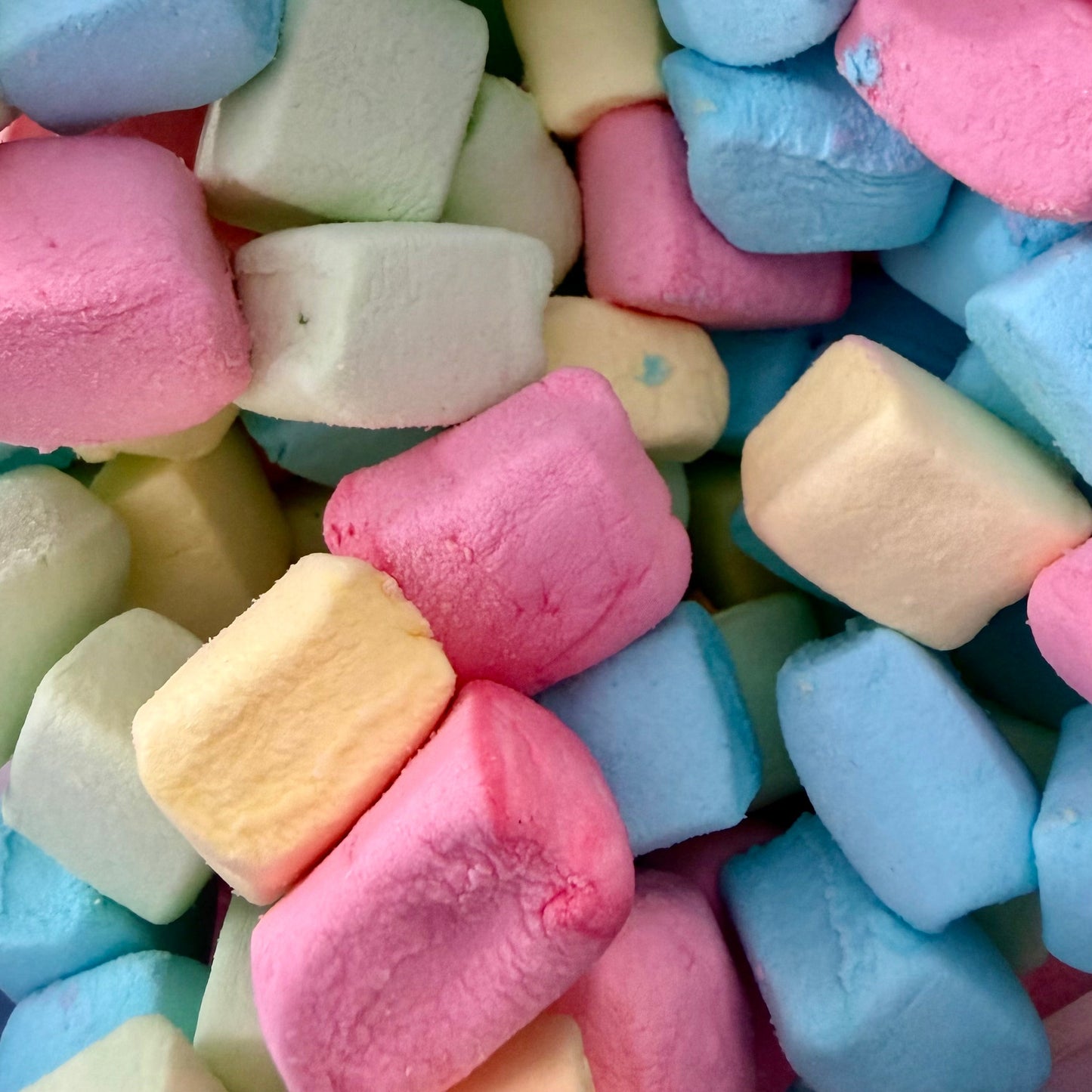 A close-up pile of pastel marshmallows in pink, light blue, pale yellow, and off-white.